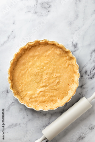 Process of making a base for shortbread pie, tart or quiche. Raw rolled dough sheet in ceramic baking form on marble background. Home baking culinary concept, recipe. Flat lay