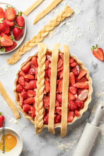 Process of making strawberry shortbread pie. Making lattice top for strawberry pie on white marble background. Home baking culinary concept, recipe. Top view
