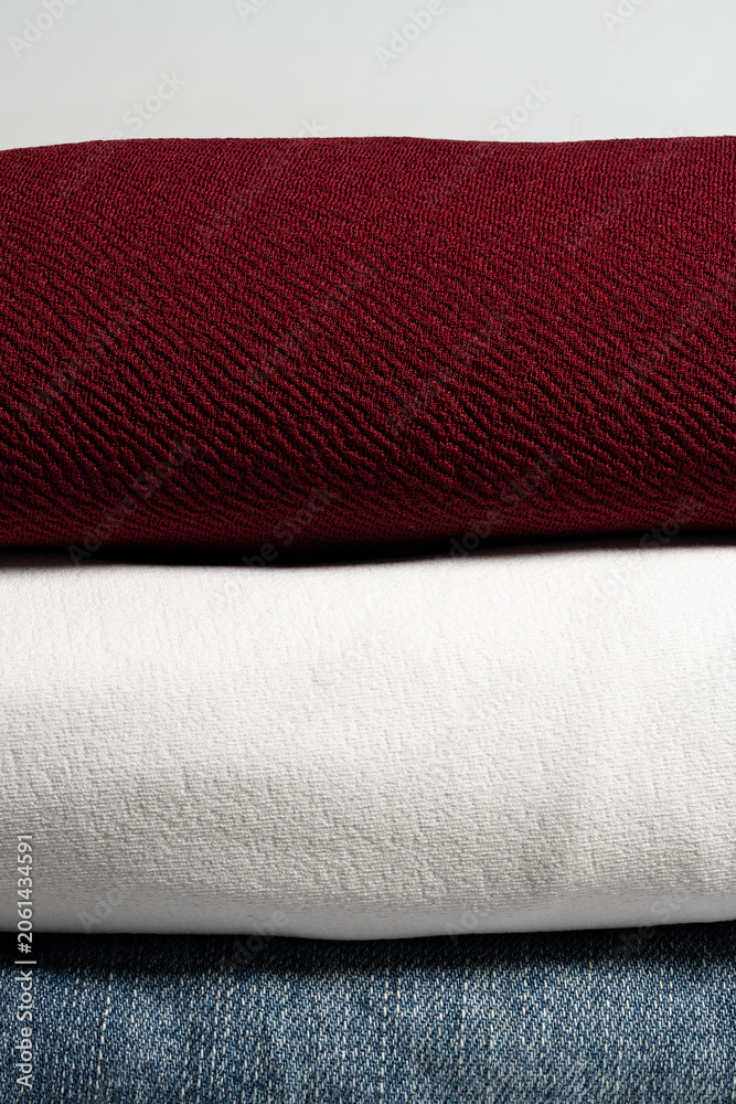 Fototapeta premium High-Resolution vertical close-up of stacked fabric layers with burgundy cotton white cloth and blue denim