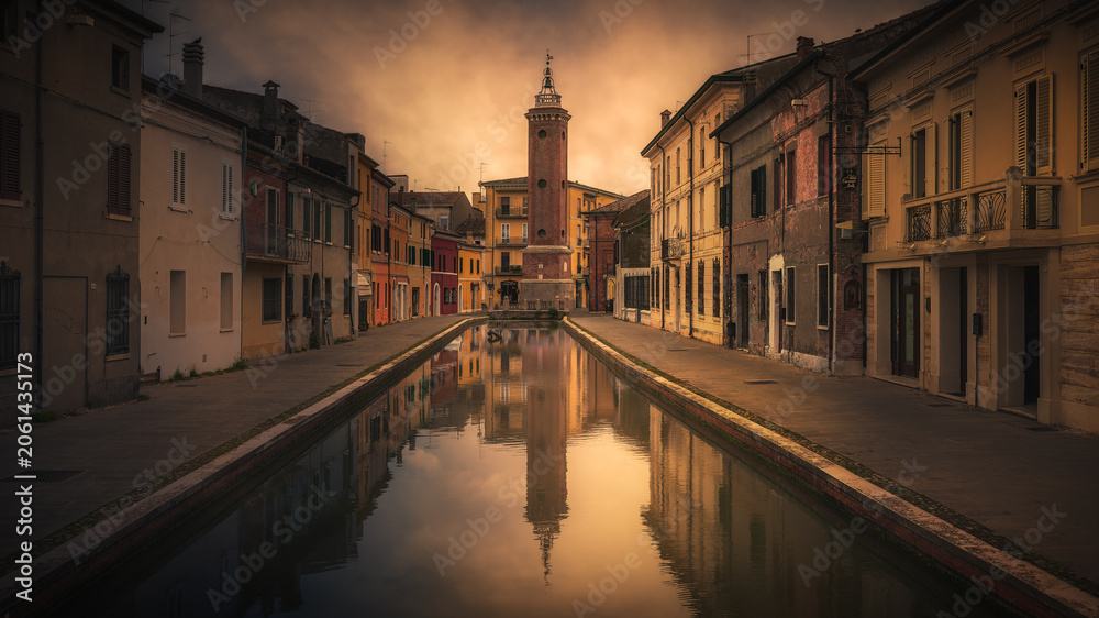 Fototapeta premium Historic Clock Tower and Canal Reflection in Comacchio at Sunset, Italy