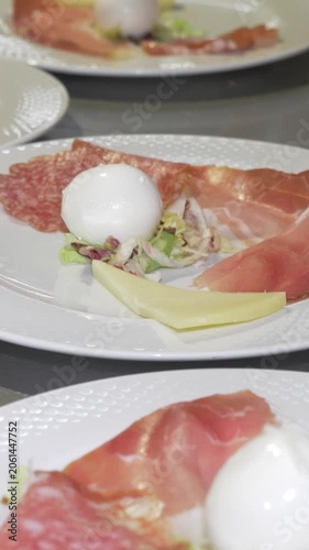 Vertical: An Italian antipasto platter nears completion, featuring creamy mozzarella, assorted cheeses and thin slices of prosciutto, a classic combination prepared for the catered party event guests.