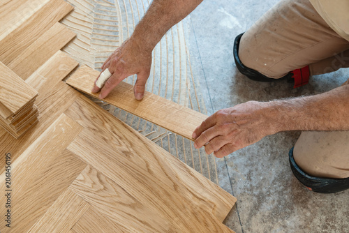 Carpenter installing herringbone wooden parquet planks during flooring work in apartment renovation