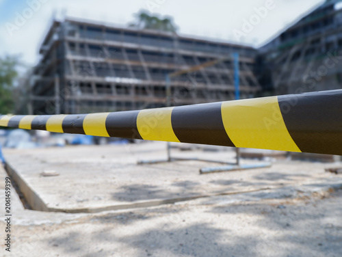 ​Yellow and black caution tape close up with blurred building construction site background, safety warning tape at industrial development area