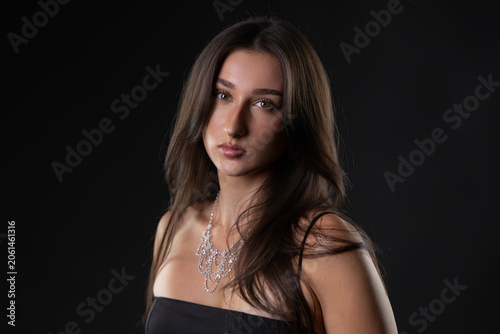 Female model wearing elegant diamond necklace with long hair posing in studio against black background