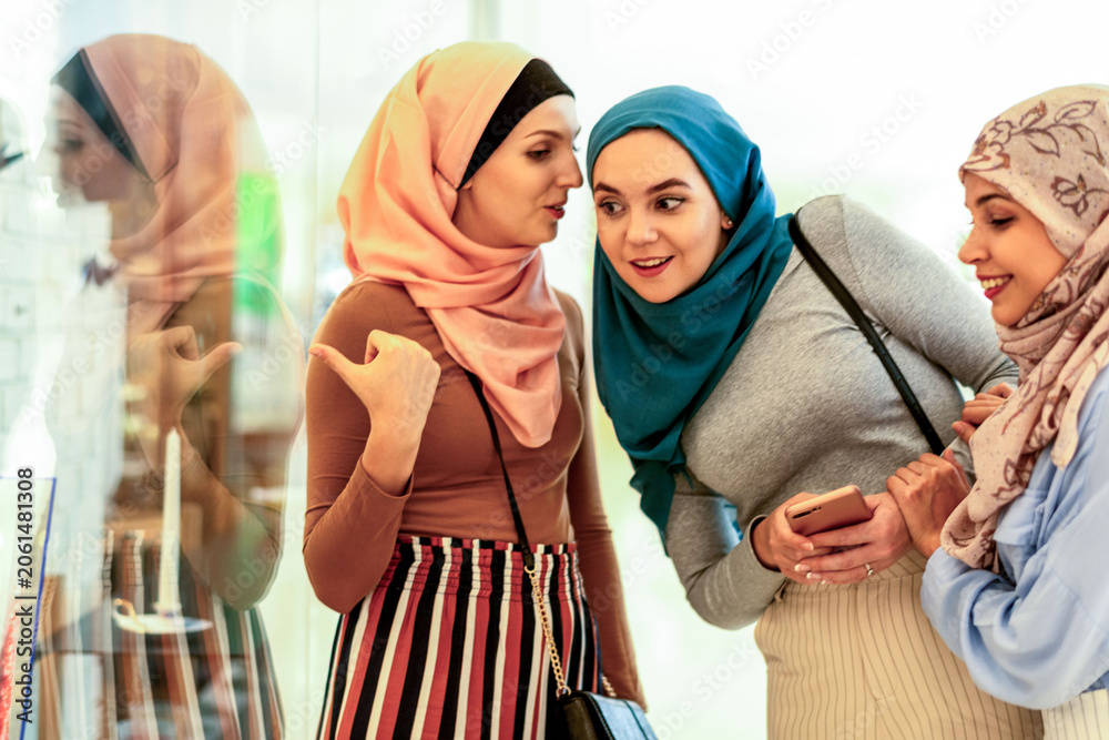 Obraz premium Three women in hijabs smiling and shopping together indoors.