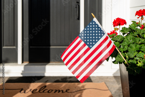 American Flag and Welcome Doormat at Front Door of House with Red Geraniums