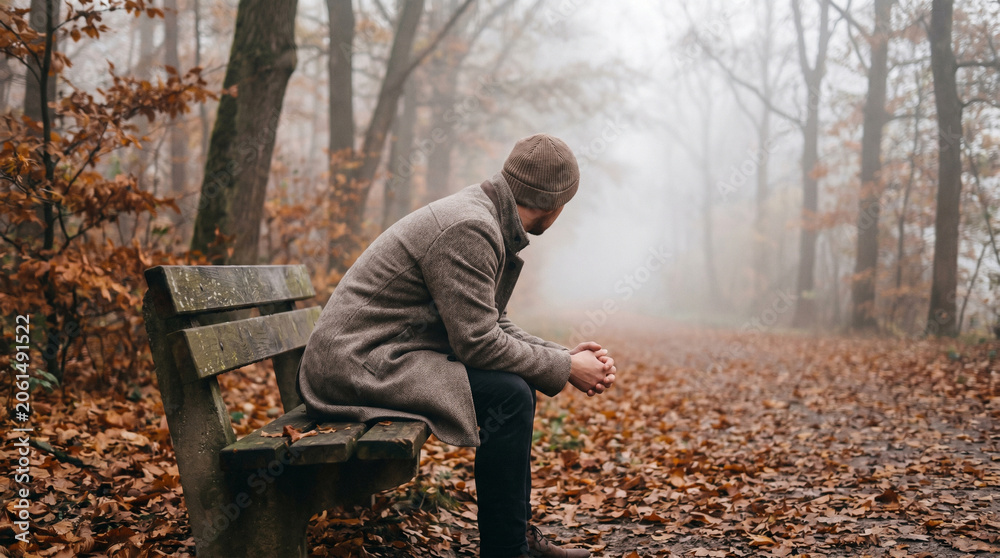 Fototapeta premium Man Sitting Alone on Park Bench Surrounded by Autumn Leaves