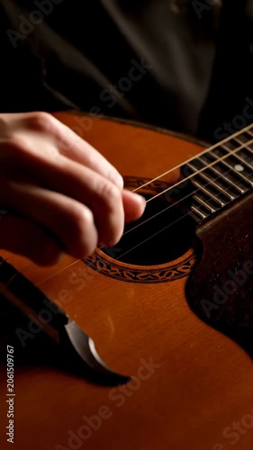 Hand playing acoustic guitar strings with close-up detail