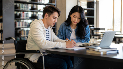 Wheelchair user studying with classmate in modern library