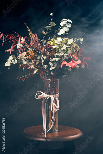 Autumn bouquet in glass vase with ribbon on stool in smoky studio