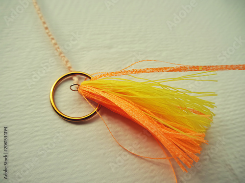 Closeup of a gold pendant with a vibrant orange and yellow tassel on a delicate chain, isolated on white background
