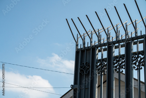 Fotografie Dark-painted metal security fence against a blue sky
