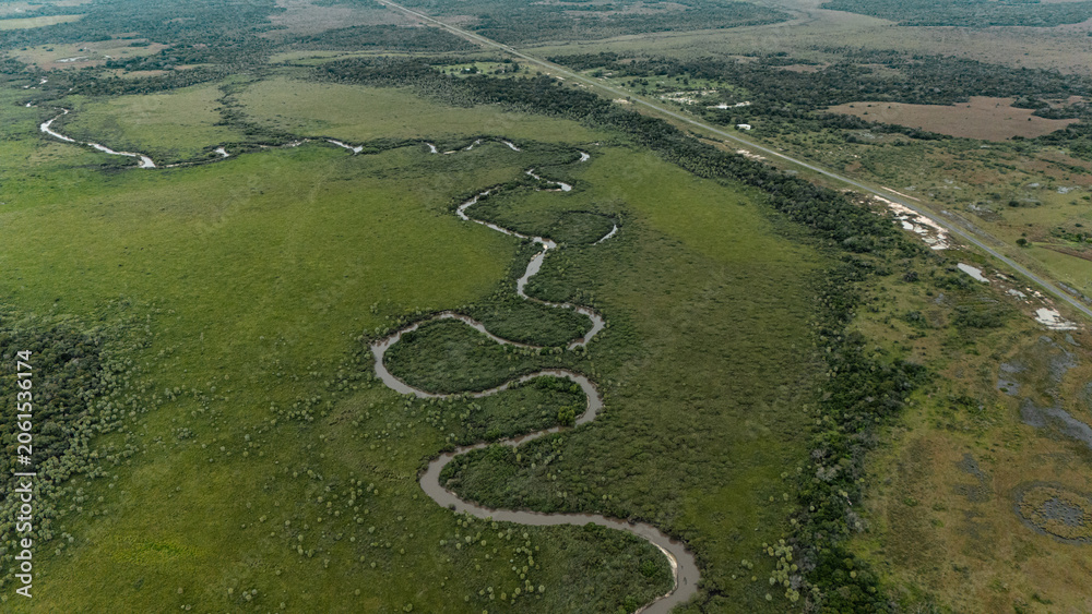 Fototapeta premium Aerial view of meandering river winding through vast green plains with highway near San Luis del Palmar, Corrientes, Argentina