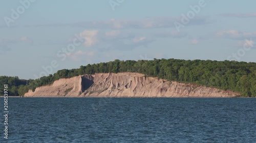 Steep sandy bluffs along the waves and lakeshore before a green forest