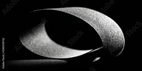 Mobius Strip Illusion: A minimalist representation of a Mobius strip, a non-orientable surface with only one surface and one boundary, cast in dramatic light and shadow.