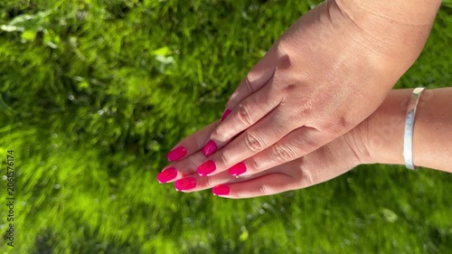 Close-up feemale hands with hygienic pink manicure on grass background, horizontal video 