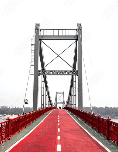 A red-painted bridge with metal railings and cables on a grey sky background