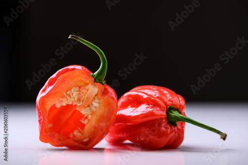 Red habanero peppers with one half cut open on dark gradient background with reflection. Fresh chili, dramatic lighting, spicy ingredient, studio shot