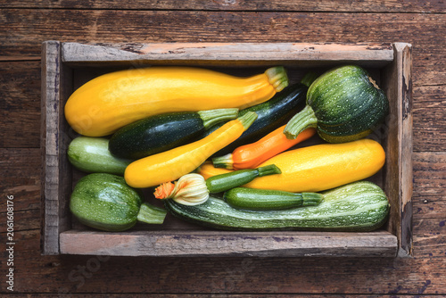 Fresh zucchini arranged in crate on wooden surface, organic vegetables composition, seasonal harvest concept. Green and yellow squash top view, natural texture, healthy food