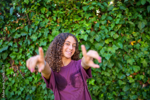 Smiling girl with wet t shirt making a hand gesture, posing outdoors in front of green ivy wall