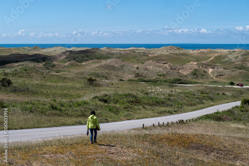 Solitary figure on rural road amid coastal dunes and open fields