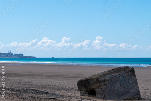 Sunlit beach scene with lone concrete structure near ocean