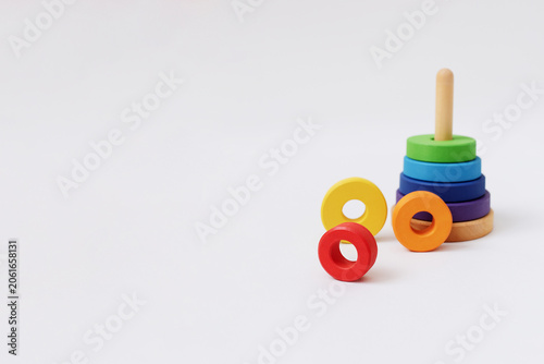 Minimalist commercial banner background with an uncompleted wooden rainbow stacking pyramid and rings on the left side, featuring large horizontal copy space on a white surface.