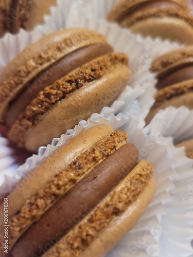 Macro shot of fresh chocolate macarons with smooth cocoa ganache filling in white paper liners, showcasing delicate crispy shells and rich texture.