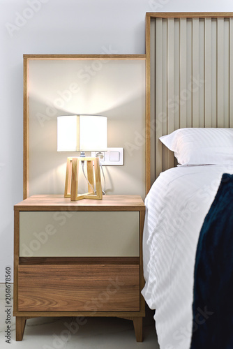 A stylish bedroom interior with contemporary bedside table, wooden lamp and white bedding. Hotel accommodation, interior design, and home decor concepts.