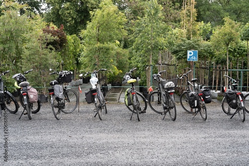 Bicycles parked in a green area near a bike parking sign on a gravel surface during daytime