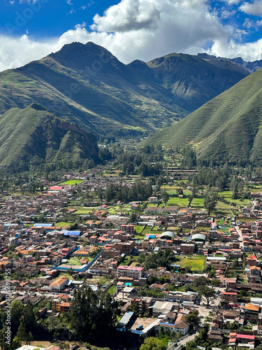 Aerial view of Urubamba in Peru’s Sacred Valley of the Incas, surrounded by lush green mountains. Traditional Andean town nestled in a fertile valley beneath dramatic clouds and breathtaking landscape