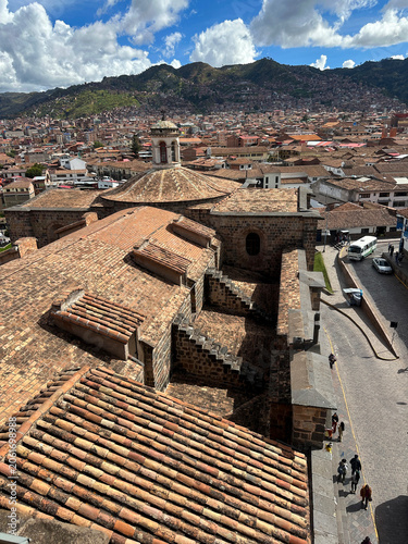 Panoramic view of Cusco, Peru, seen from the historic Sacsayhuamán archaeological site. The ancient Inca capital spreads across a mountain valley, surrounded by dramatic Andean landscapes and clouds.