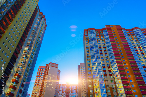 Low angle view of modern colorful high rise residential apartment buildings in a new district at golden hour sunset with sun flare and blue sky