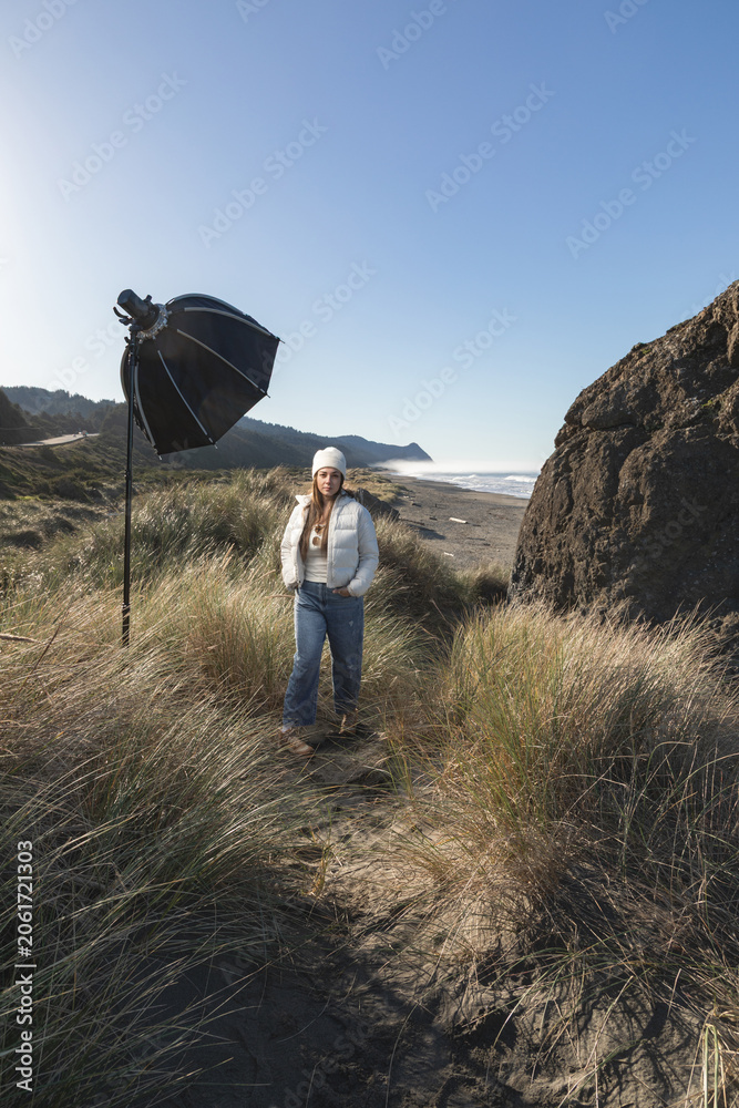 Obraz premium Woman stands on a sand dune in Gold Beach Oregon, with a strobe and softbox for a photoshoot.