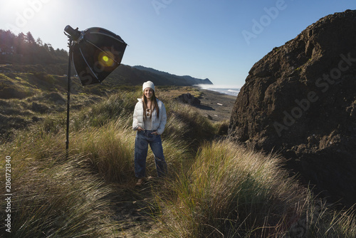Woman stands on a sand dune in Gold Beach Oregon, with a strobe and softbox for a photoshoot.