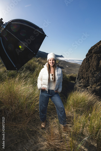 Woman stands on a sand dune in Gold Beach Oregon, with a strobe and softbox for a photoshoot.