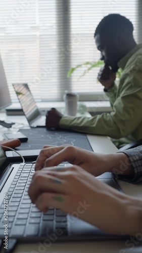 Vertical rack focus shot of diverse young adult developers typing on laptops in office. Footage ideal for commercial use in IT recruitment, software development ads, corporate tech presentations