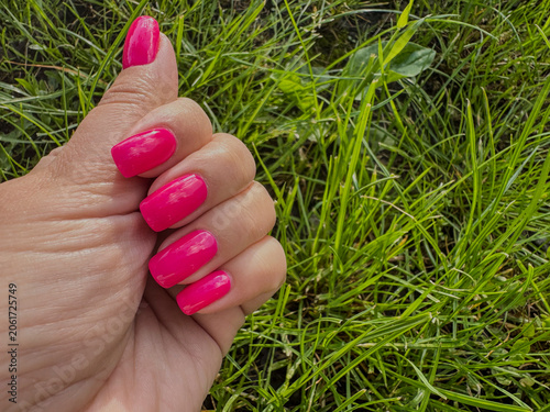 Close-up feemale hand with pink gel polished manicure on grass background