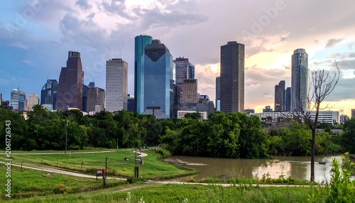 A serene cityscape with a park and pond in the foreground, surrounded by a lush green landscape and towering skyscrapers in the background