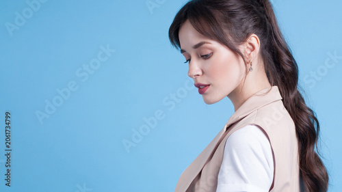 Young woman looking down posing in blue studio background