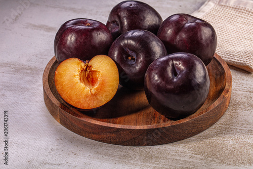 Φωτογραφία ripe dark purple plums on wooden plate with one cut open