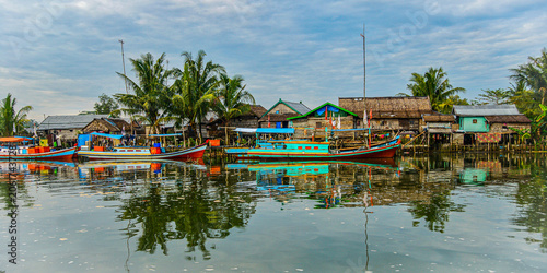 Traditional fishing boats and waterfront homes reflected in calm waters at a coastal village in East Belitung, Indonesia. Tropical maritime culture and island lifestyle destination.