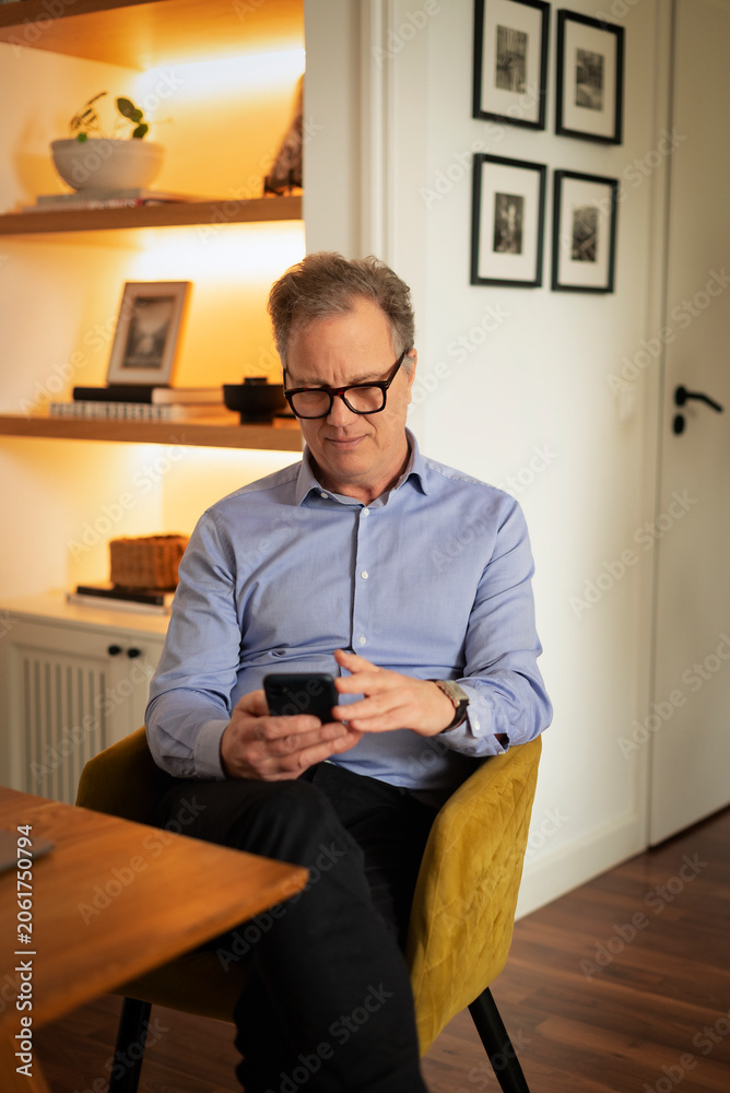 Fototapeta premium Mature man using smartphone while sitting at home