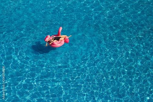 Woman on flamingo pool float in pool, drone aerial view. Summer holidays, copy space, space for text