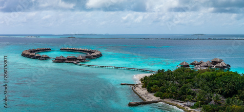Foto Aerial view of a Maldives luxury resort shows a circular ring of overwater villas linked by a long wooden boardwalk to a palm island, with turquoise to sapphire seas and white sand