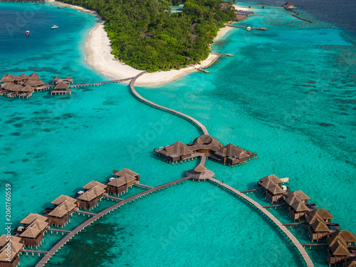 Quadro em tela Aerial view of a Maldives luxury resort shows overwater villas on curved wooden boardwalks, a white sand beach, and a palm island under bright midday tropical light