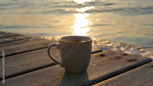 Hot Coffee Mug Steaming on a Wooden Pier by the Sea at Sunset. Seamless looping 4k video background