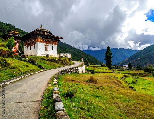 A serene mountainous landscape featuring a traditional white and brown building with a dark roof situated on a hillside beside a winding road