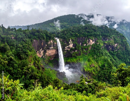 A serene waterfall cascades down a lush green mountain slope (1)