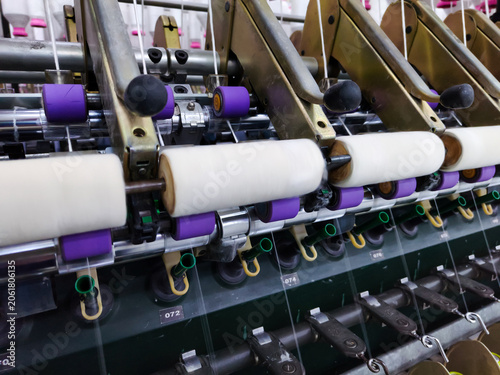 Close up of spinning rollers with white cotton thread on automated textile machinery in industrial factory